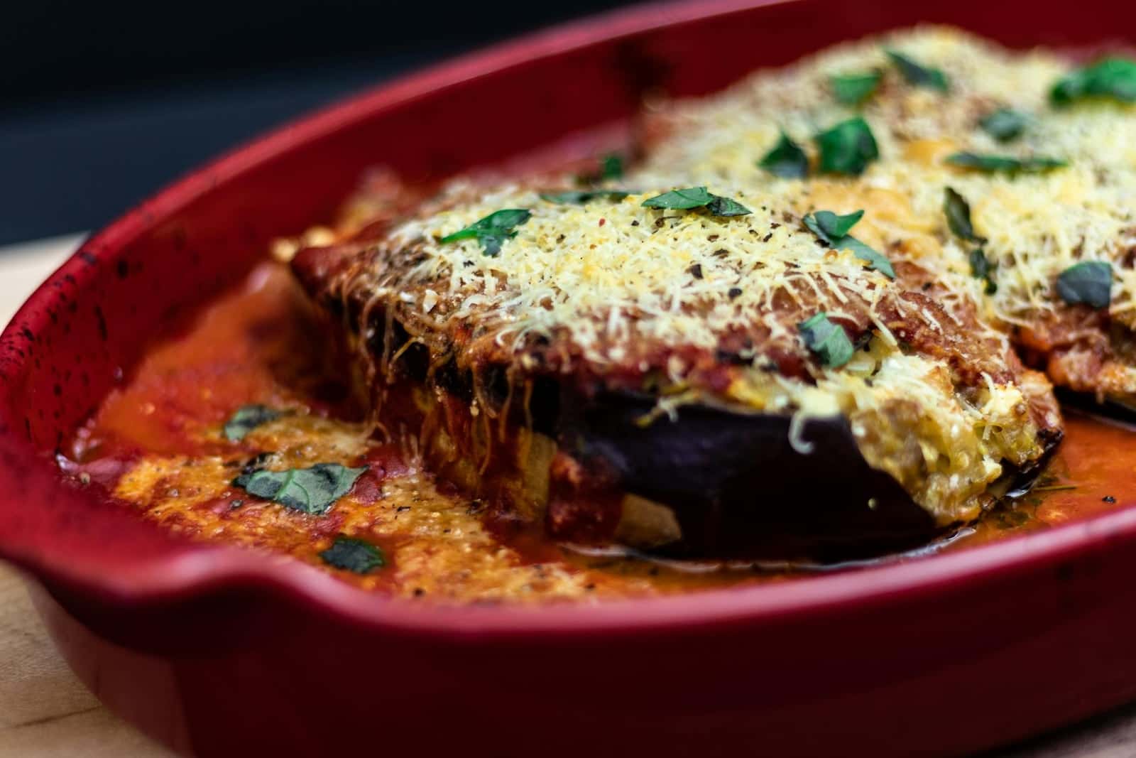 Eggplant Parmesan baked with tomato sauce, melted cheese, and herbs in a red dish