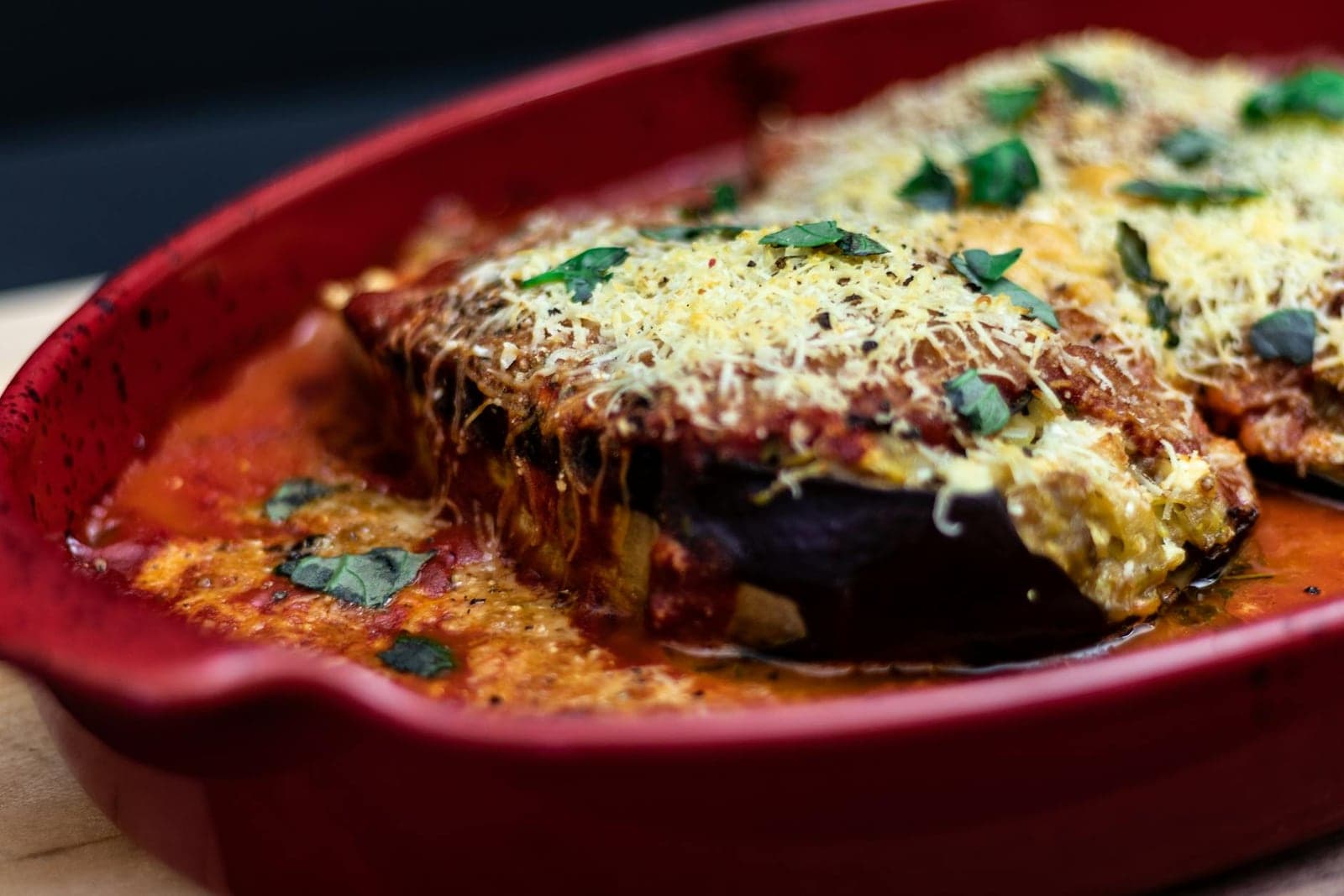 Eggplant Parmesan baked with tomato sauce, melted cheese, and herbs in a red dish
