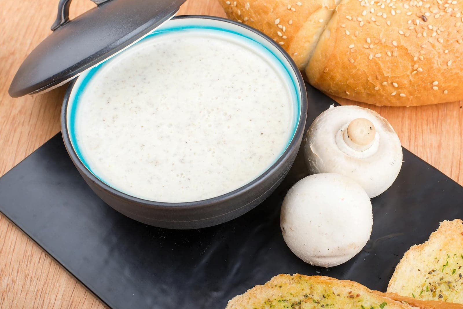 Cream of mushroom soup in a bowl with bread and garlic toast on a wooden surface