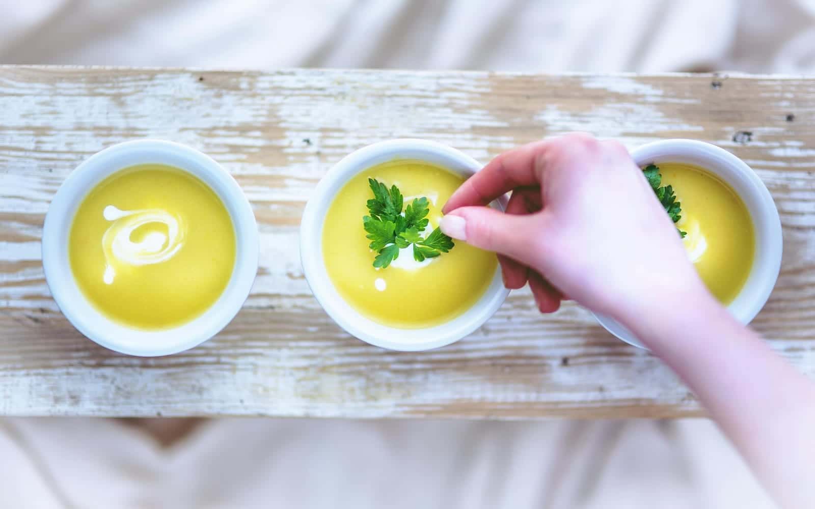 Creamy baked potato soup bowls being garnished with herbs