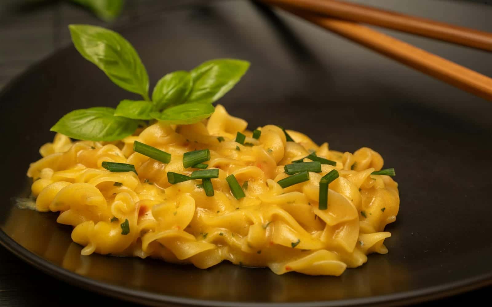 Creamy lemon pasta with yellow sauce, herbs, and short noodles in a dark bowl