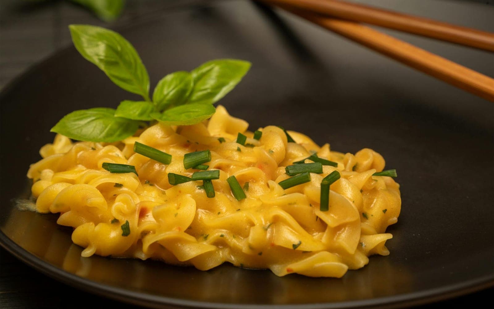 Creamy lemon pasta with yellow sauce, herbs, and short noodles in a dark bowl