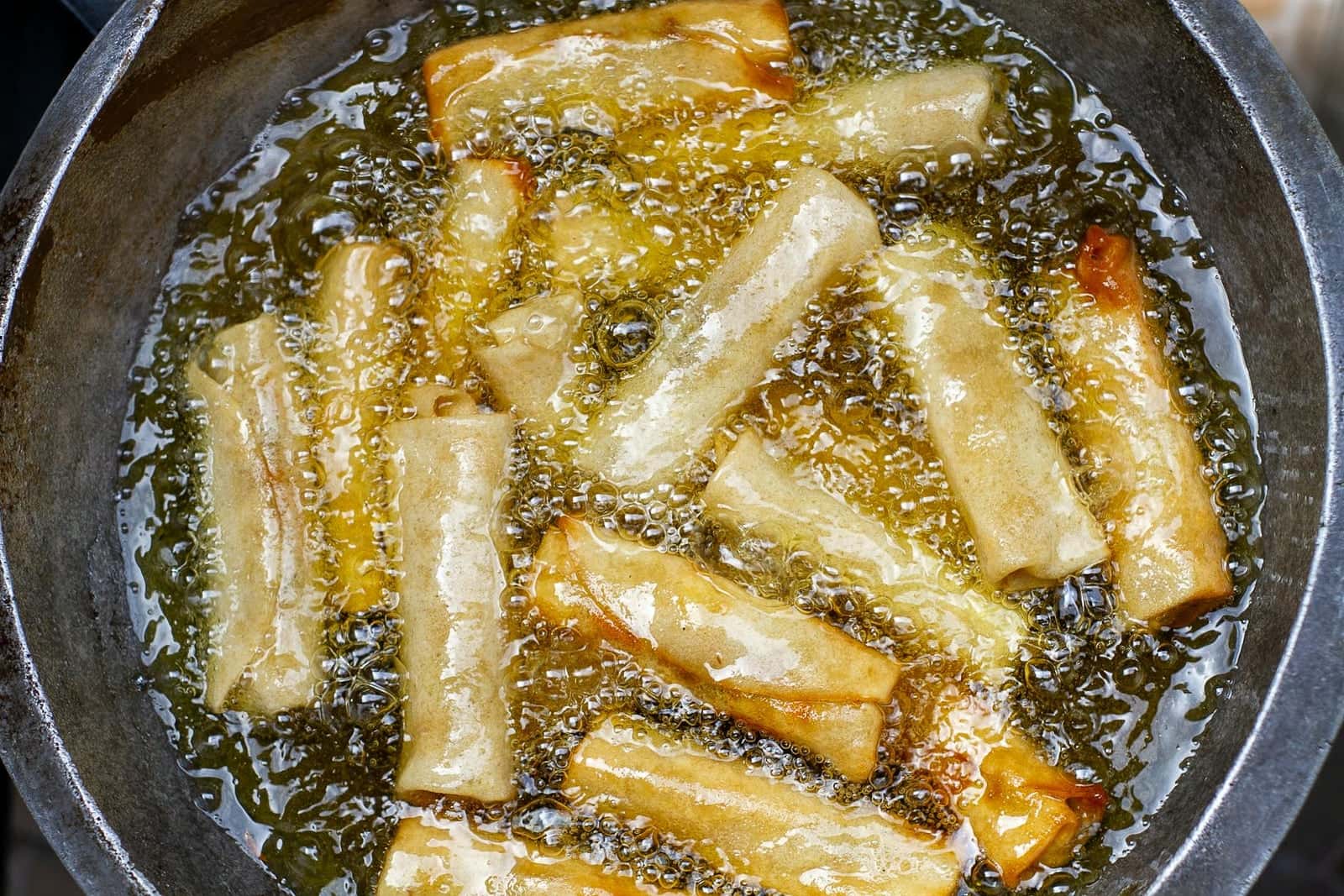 Crispy pork spring rolls frying until golden with bubbled wrappers