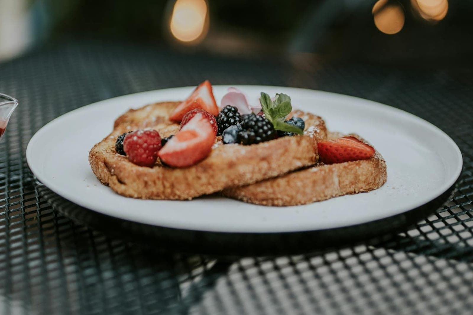 Croissant French toast topped with strawberries, blackberries, and cream on a white plate