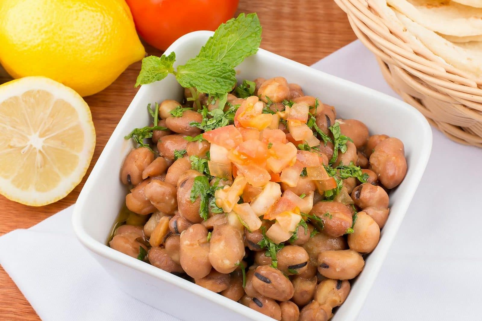 Ful medames breakfast bowl with fava beans, lemon, tomato, onion, and fresh herbs