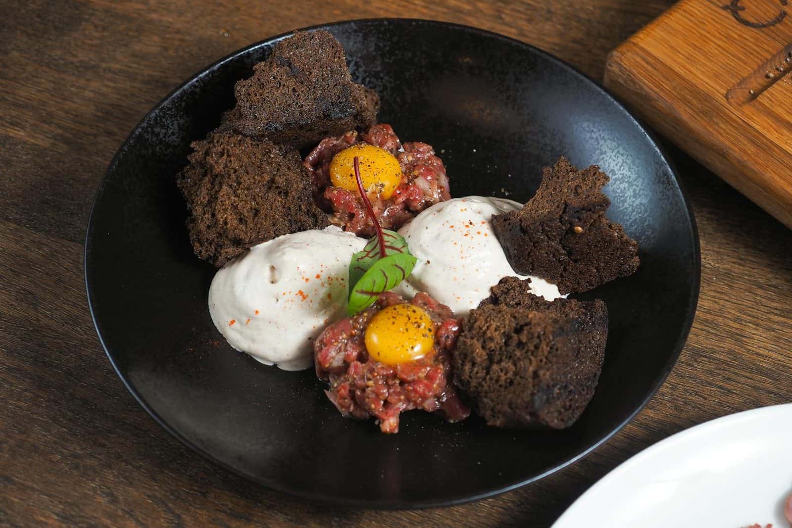 Kitfo-style seasoned minced beef tartare plated with soft egg and small crisp garnishes
