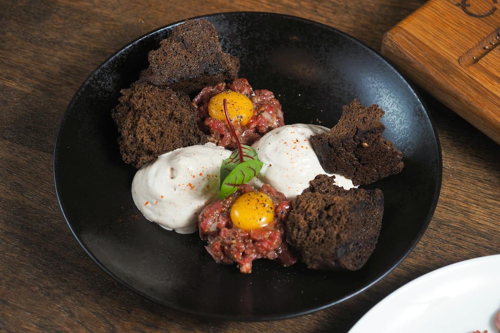 Kitfo-style seasoned minced beef tartare plated with soft egg and small crisp garnishes