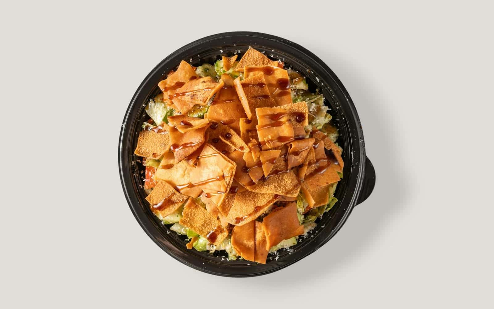 Fattoush crouton salad with crisp pita pieces, vegetables, and dressing in a black bowl