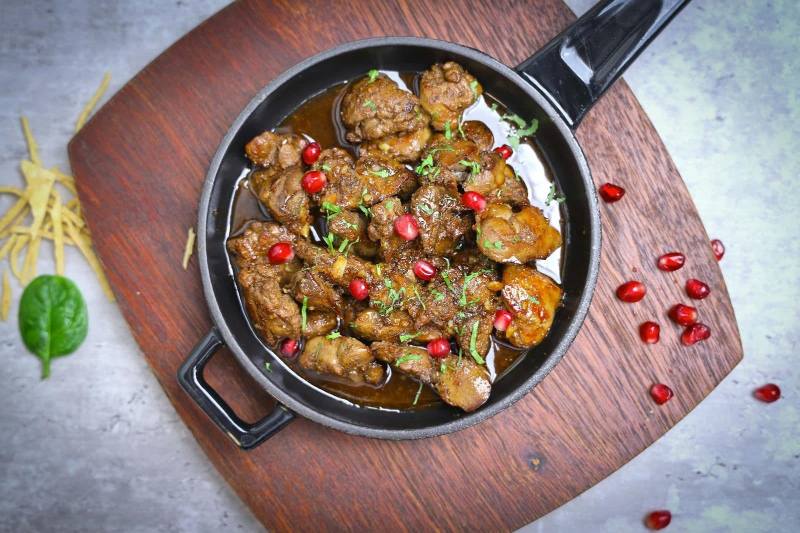 Fesenjan-style walnut pomegranate stew in a black pan with glossy sauce and pomegranate seeds