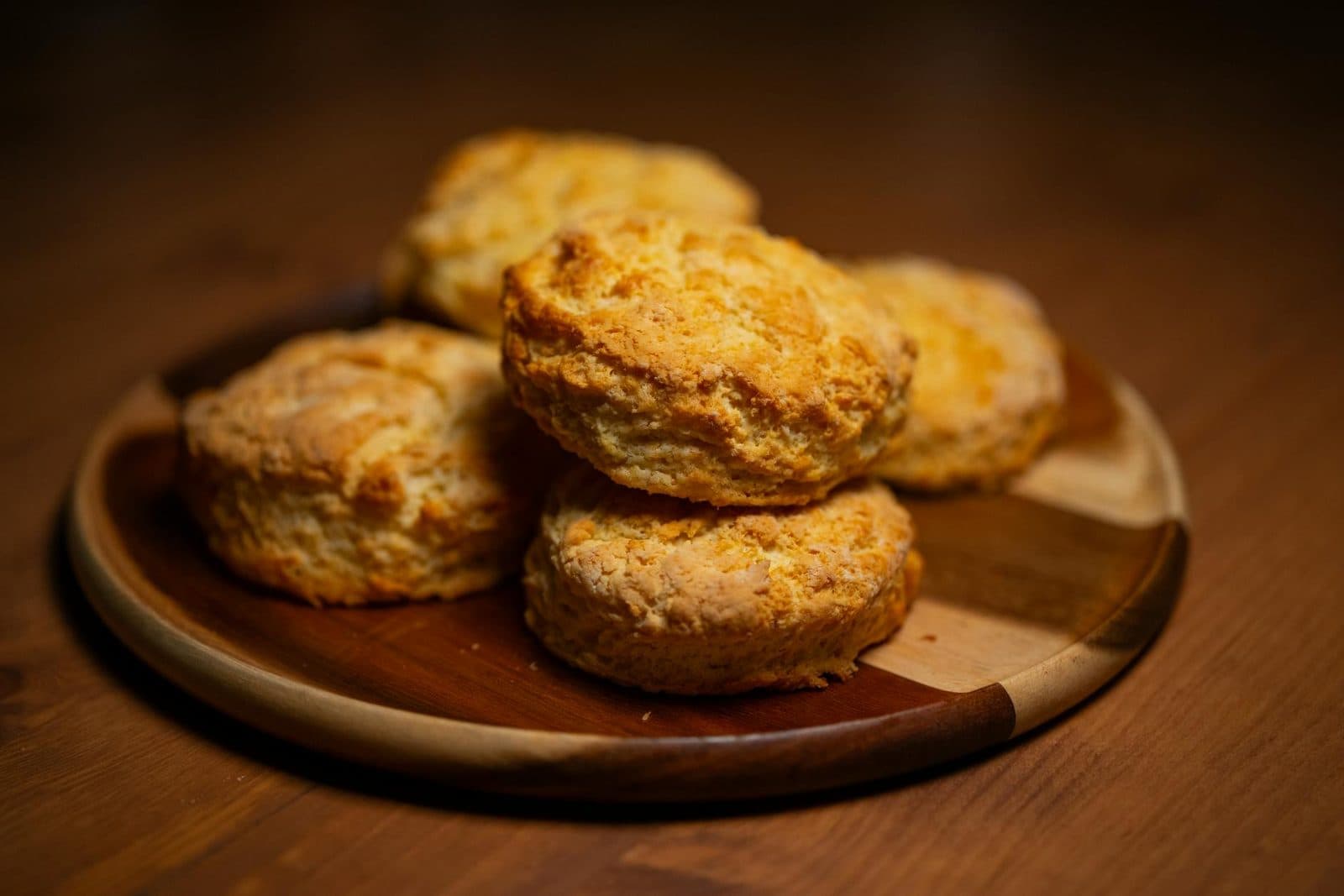 Fluffy buttermilk biscuits stacked on a wooden plate with golden craggy tops