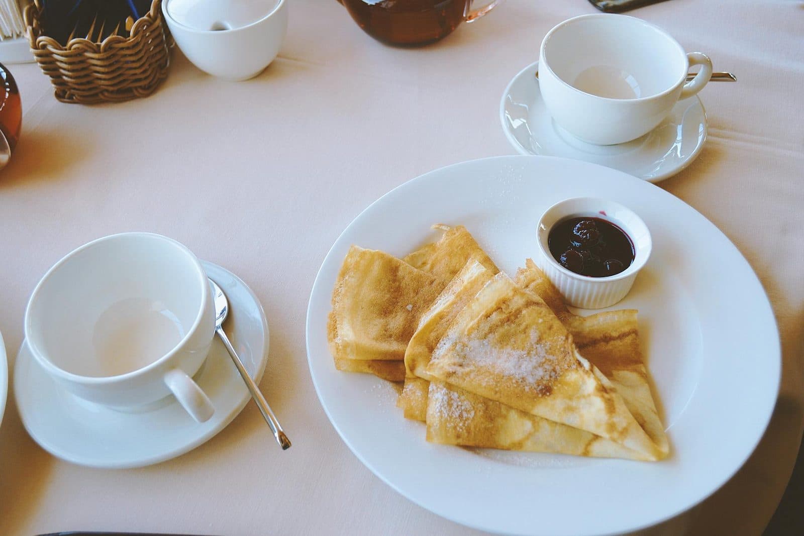 French crepes dusted with powdered sugar beside tea on a bright breakfast table