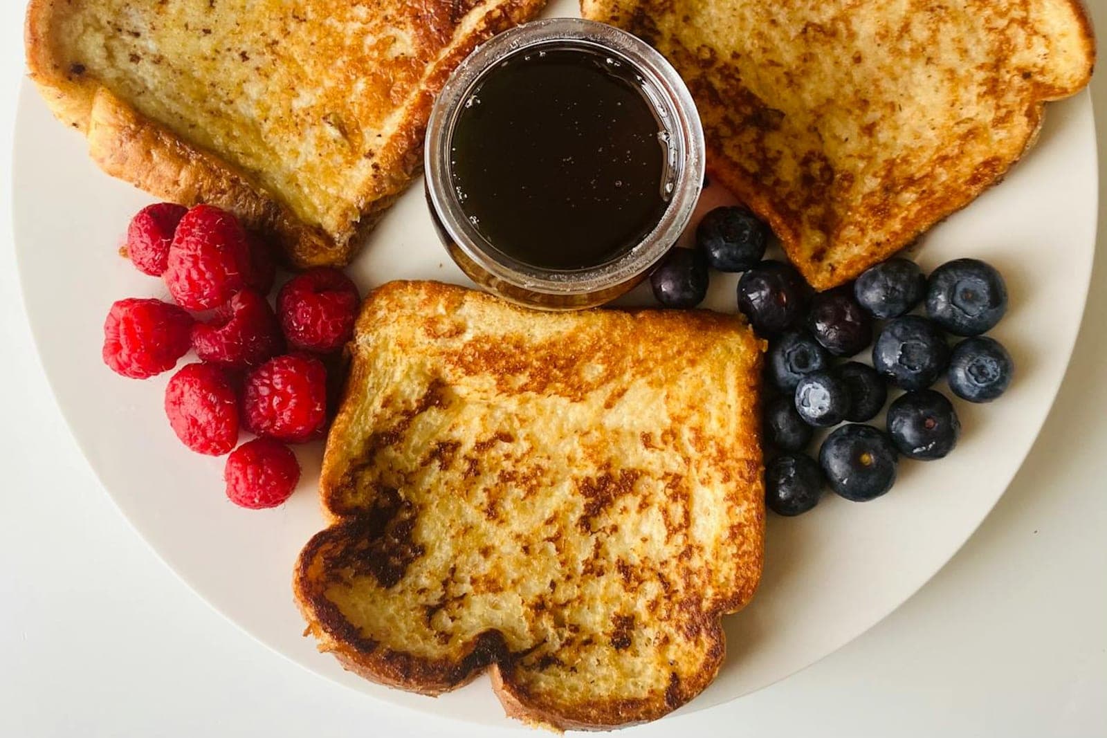 Berry French toast bake-style slices with blackberries, raspberries, blueberries, and syrup