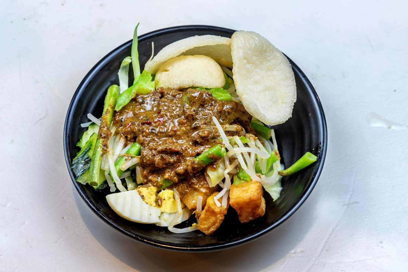 Indonesian gado gado salad bowl with vegetables, tofu, peanut sauce, and crisp garnish