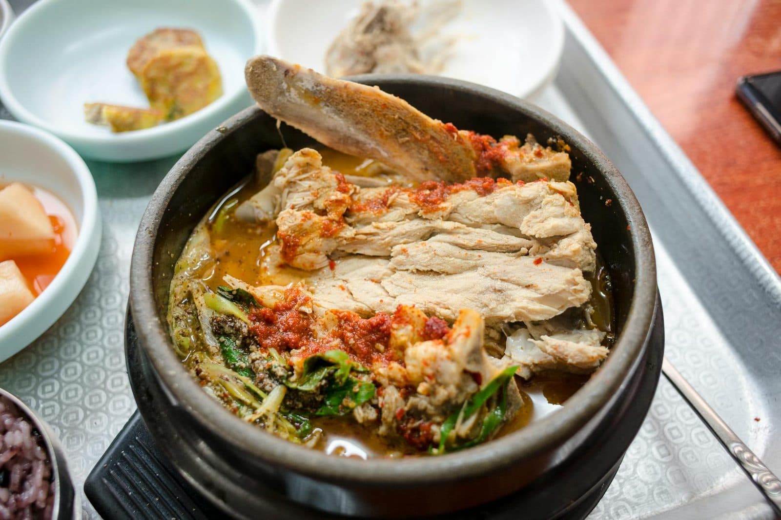 Korean gamjatang pork bone stew in a clay pot with broth, vegetables, and side dishes
