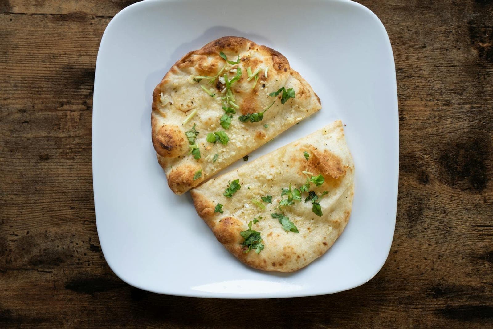 Garlic naan bread pieces brushed with herbs and served on a white plate