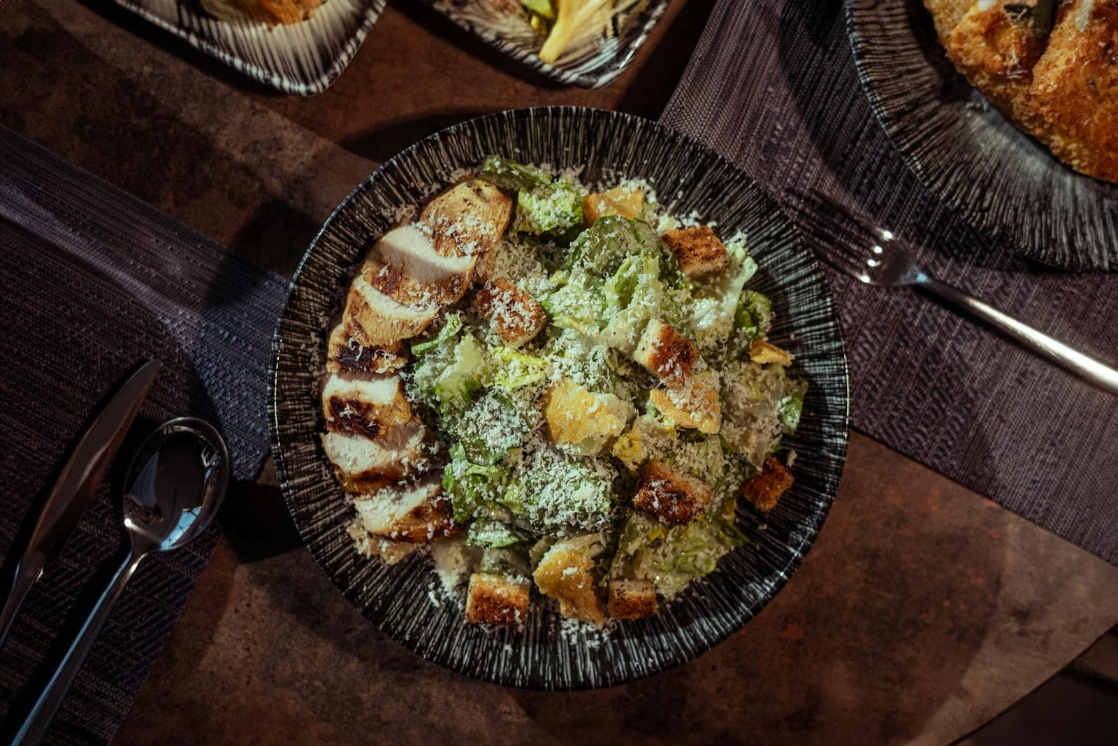 Grilled chicken Caesar salad with romaine, croutons, and parmesan in a dark bowl