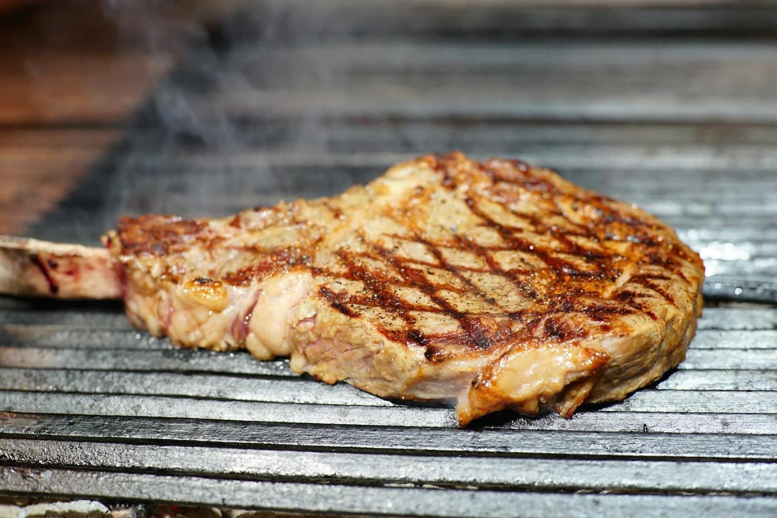 Grilled ribeye steak with charred crust and smoke rising from the barbecue