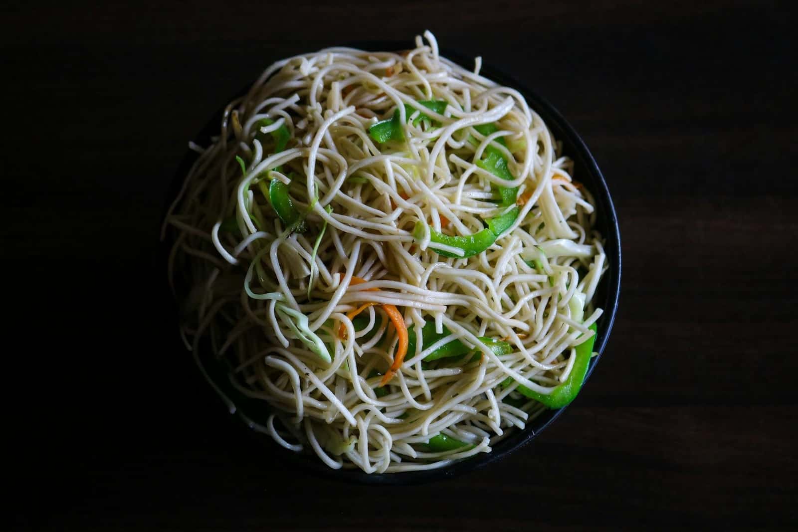 Hakka noodles stir-fried with vegetables and served in a dark bowl