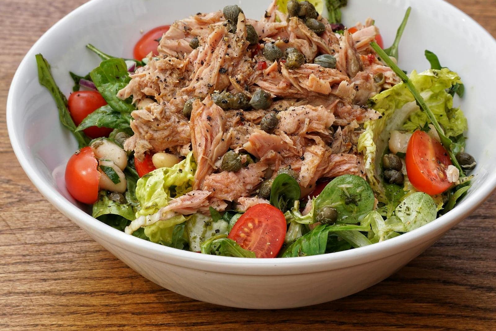 Mediterranean tuna and white bean salad with tomatoes, greens, capers, and herbs in a bowl