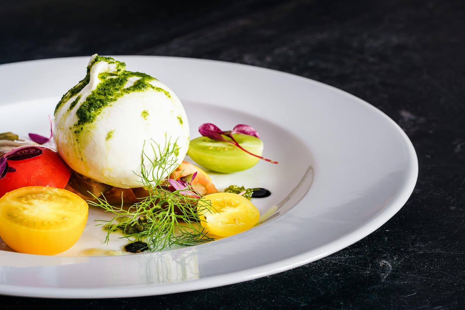 Heirloom tomato and burrata salad with pesto, herbs, and colorful tomatoes on a white plate