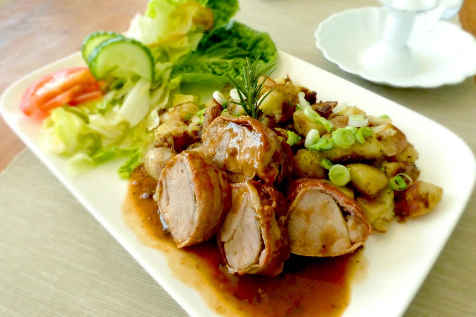 Herb-roasted pork tenderloin sliced with potatoes, rosemary, and a fresh salad