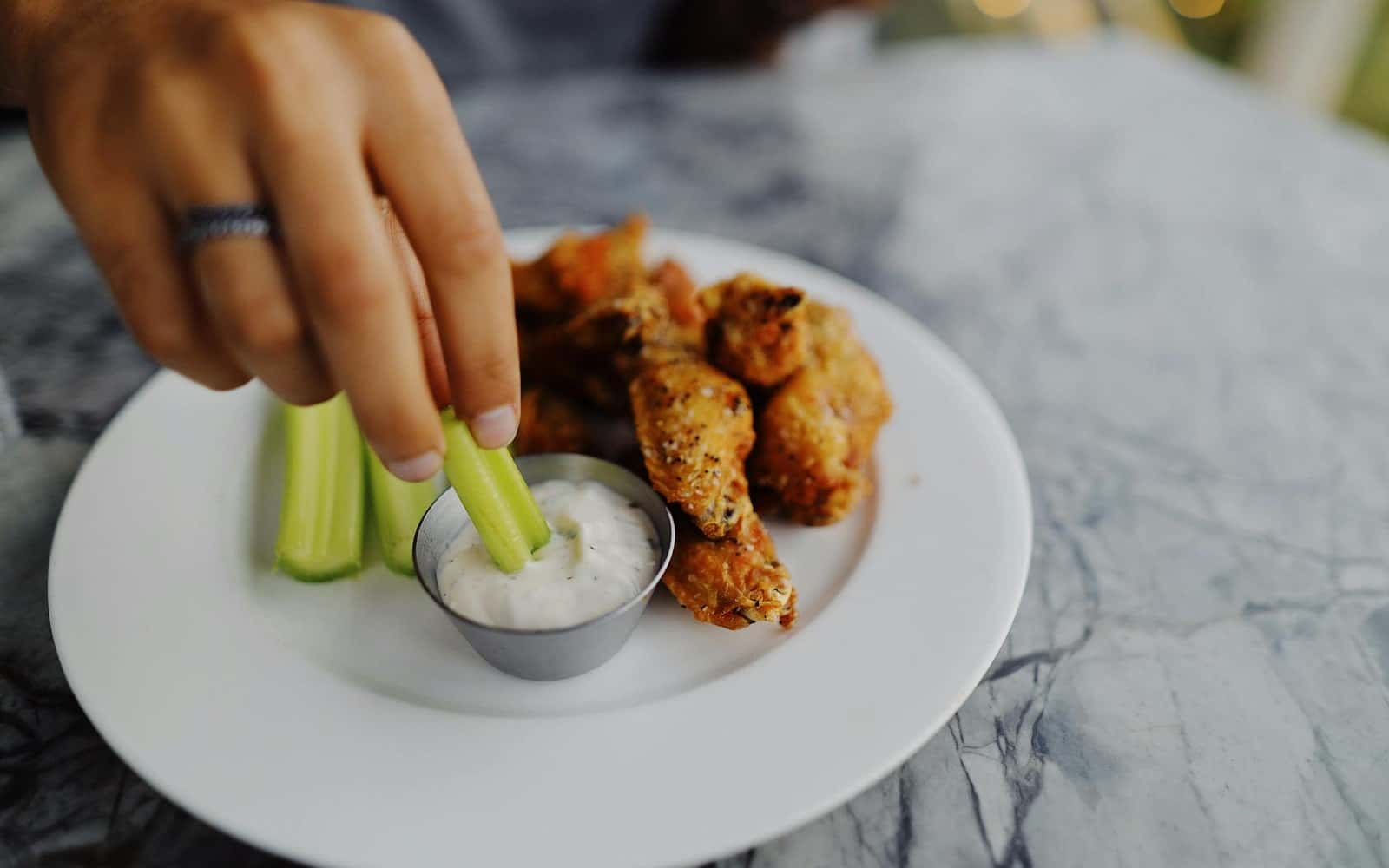 Homemade ranch dressing with celery and chicken wings on a white plate
