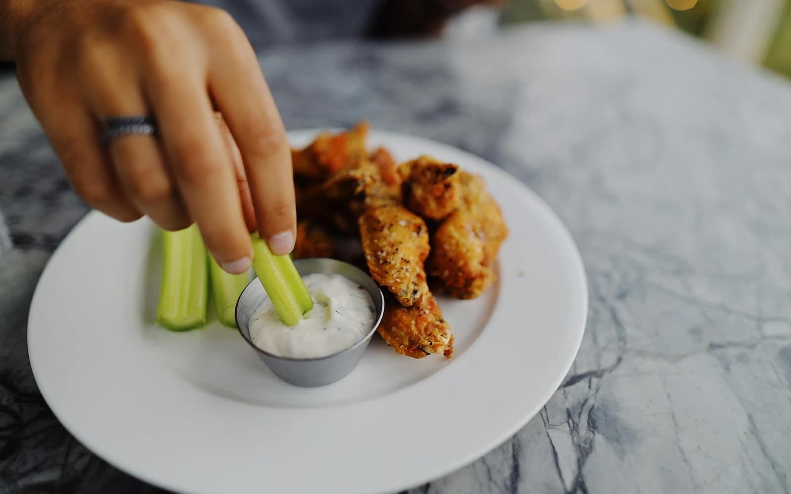Homemade ranch dressing with celery and chicken wings on a white plate
