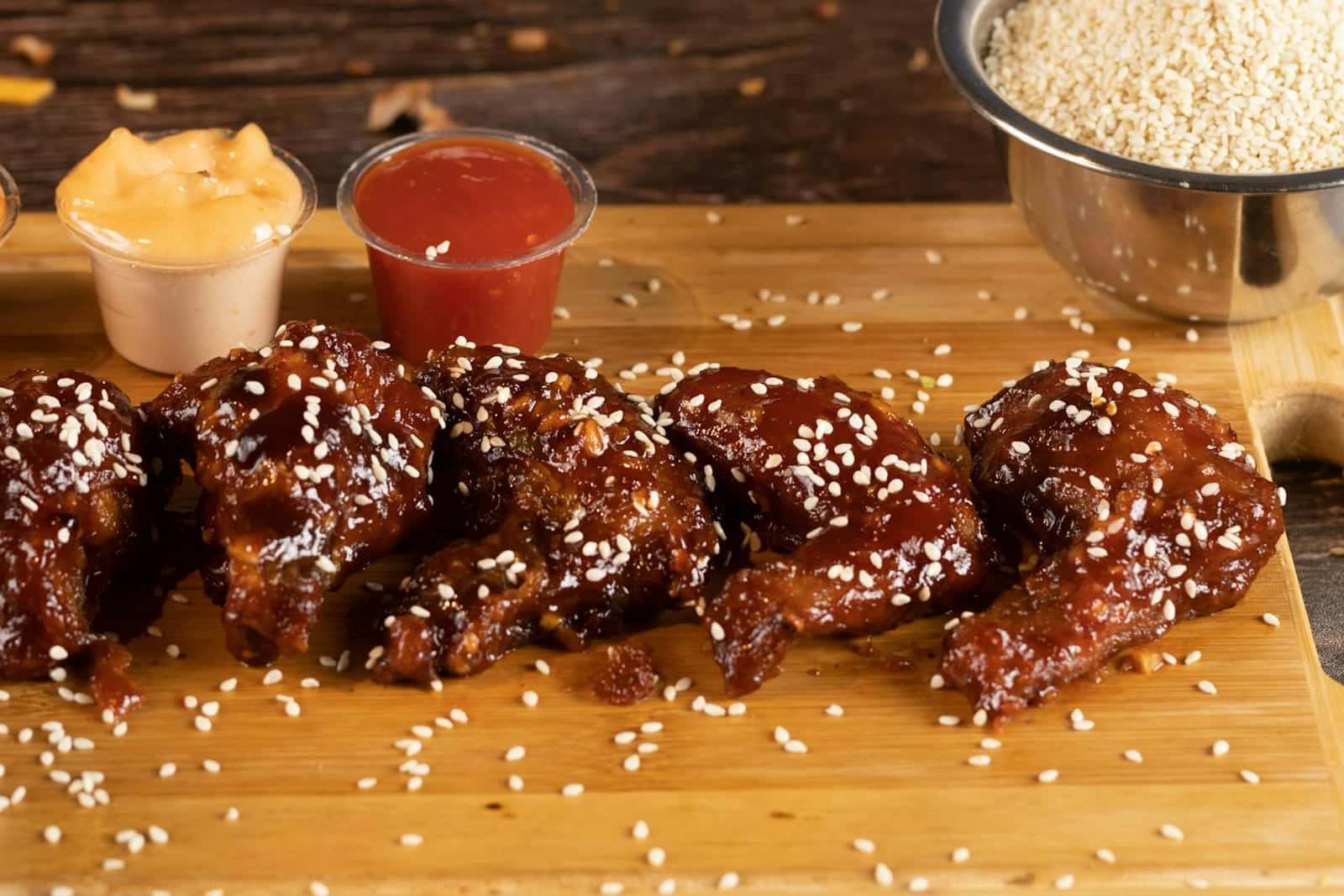 Honey sriracha chicken wings glazed with sauce and sesame seeds on a wooden board