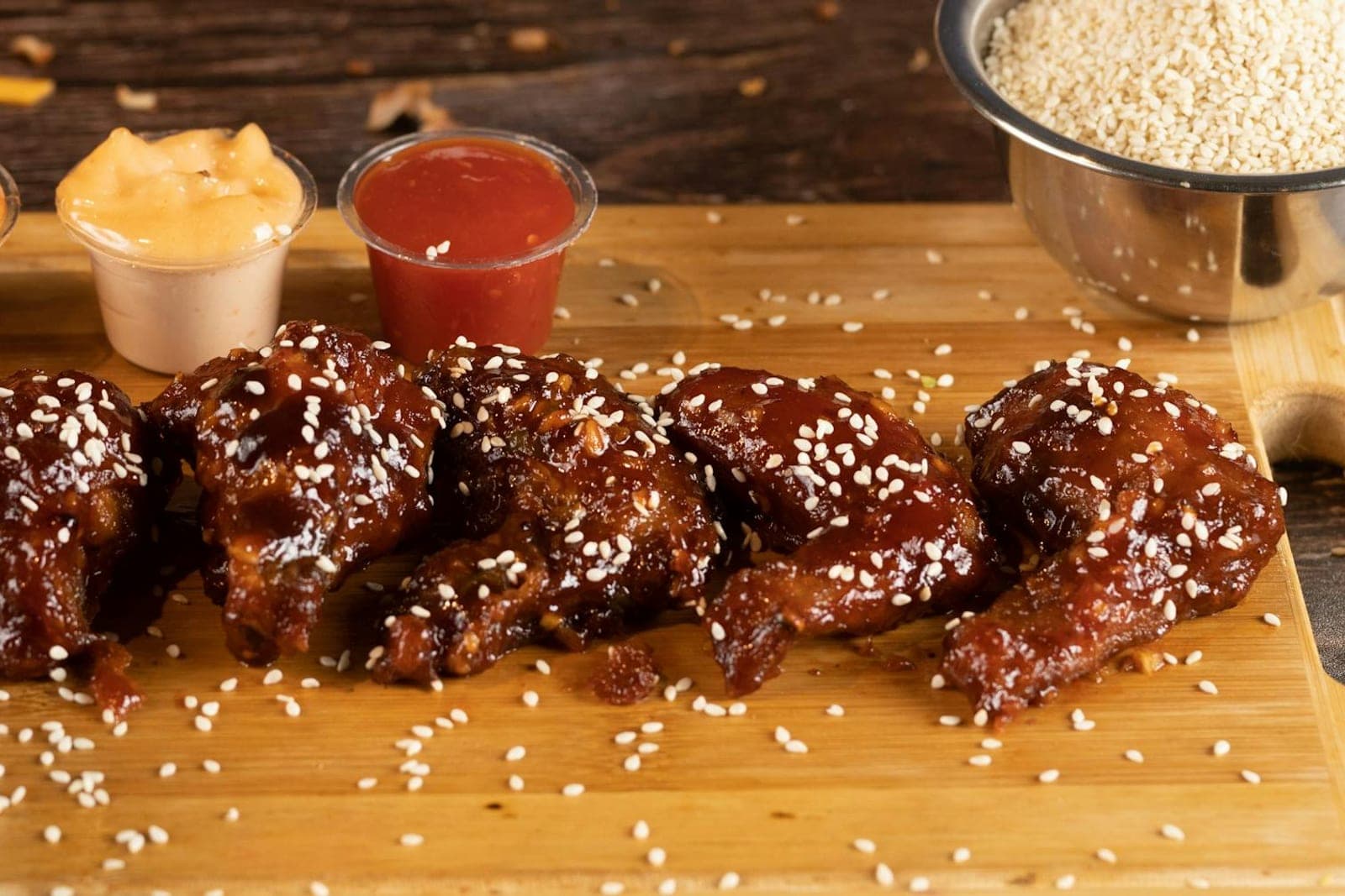 Honey sriracha chicken wings glazed with sauce and sesame seeds on a wooden board
