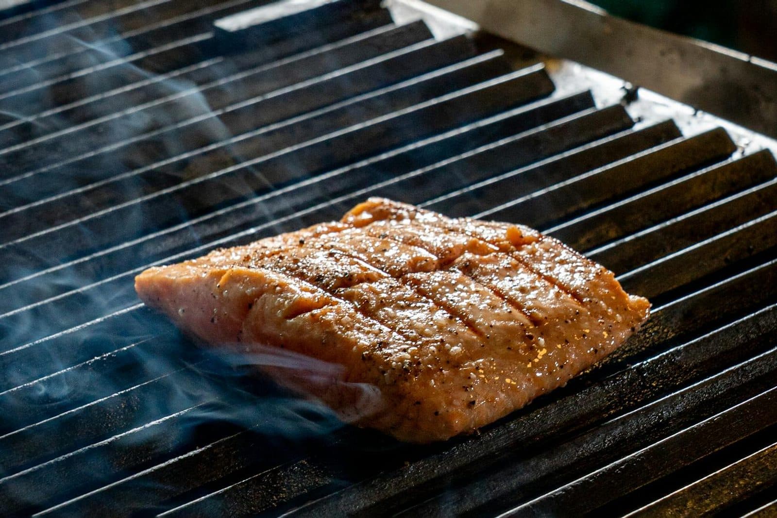 Hot smoked salmon fillet on an outdoor grill surrounded by aromatic smoke