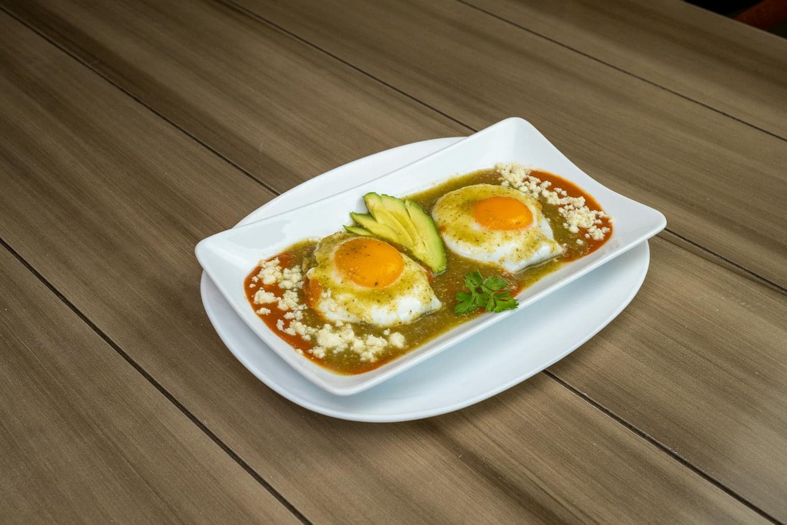 Huevos rancheros with eggs, salsa, avocado, and cheese on a white platter