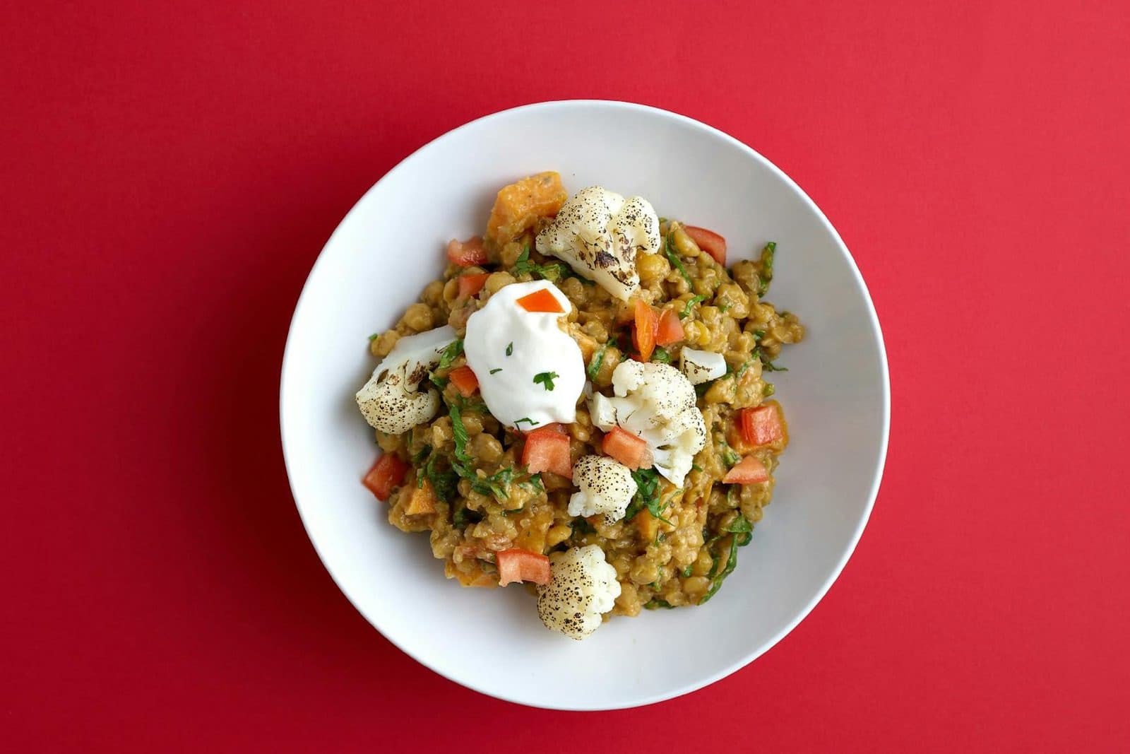 Indian butter cauliflower curry with vegetables and spices in a white bowl on a red background