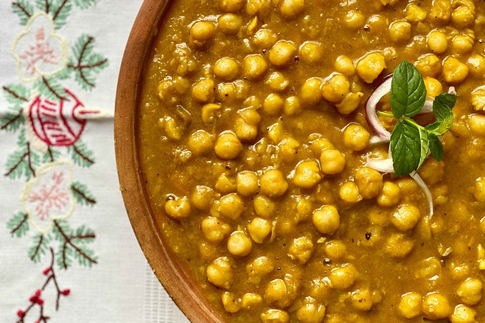 Indian chana masala stew with chickpeas, curry sauce, mint, and sliced red onion in a bowl
