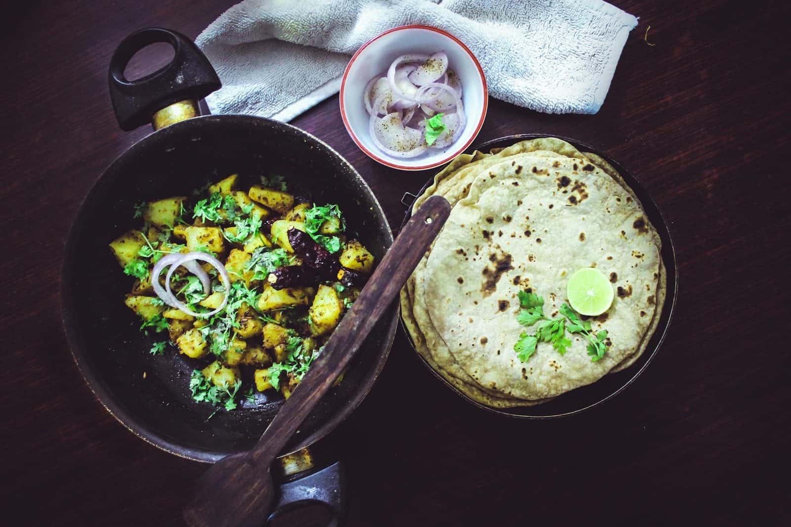 Indian jeera aloo potatoes with roti, onions, lime, and herbs in a black skillet