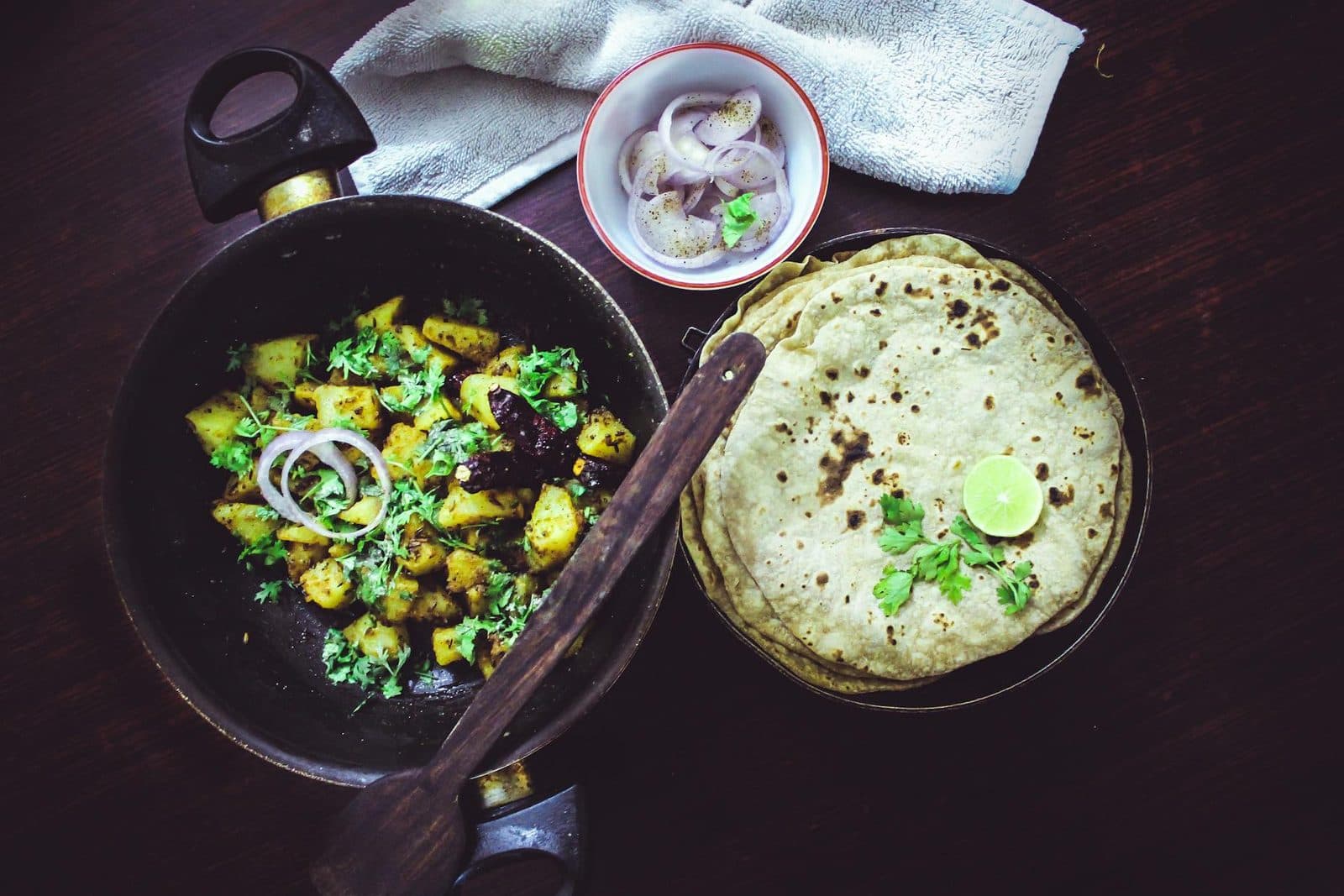 Indian jeera aloo potatoes with roti, onions, lime, and herbs in a black skillet