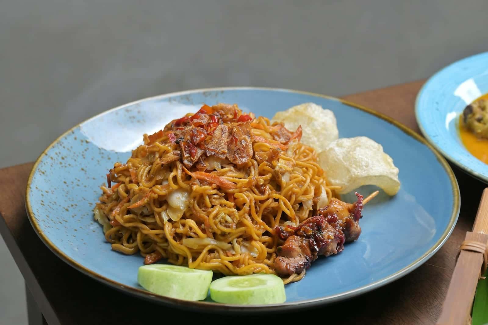 Indonesian mie goreng noodles with cucumber, lime, crackers, and savory sauce on a blue plate