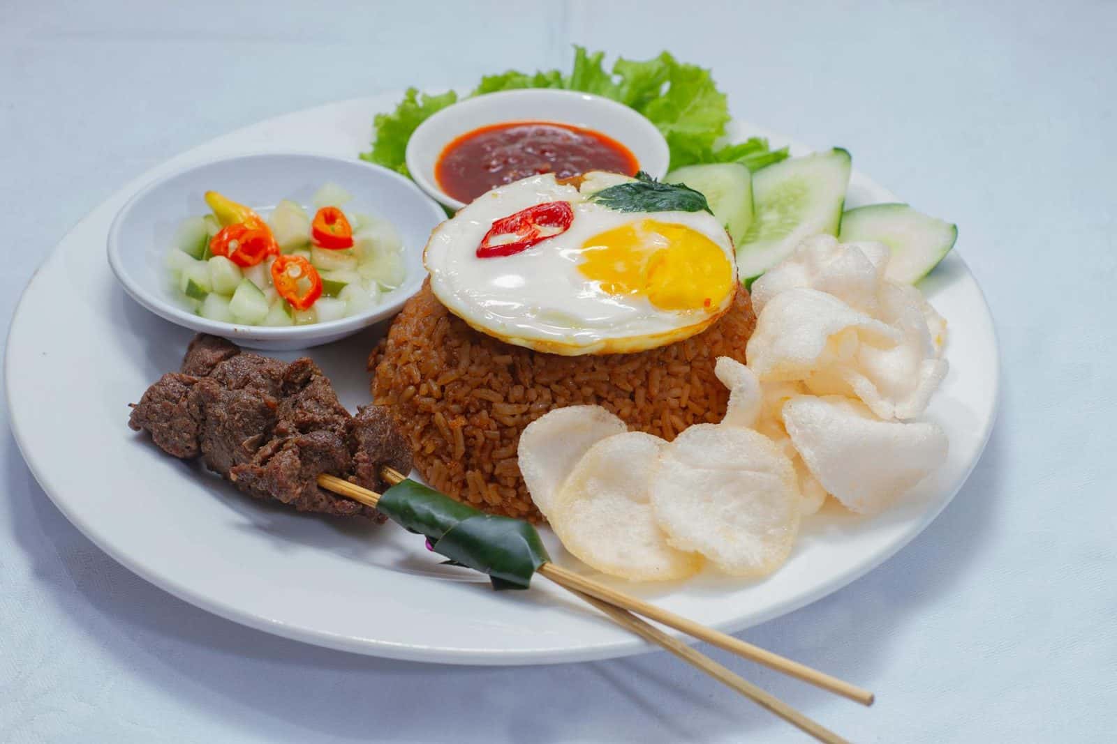 Indonesian nasi goreng fried rice with egg, crackers, cucumber, and sambal on a white plate