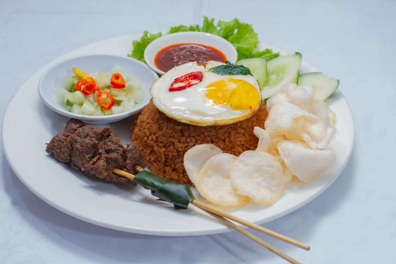 Indonesian nasi goreng fried rice with egg, crackers, cucumber, and sambal on a white plate
