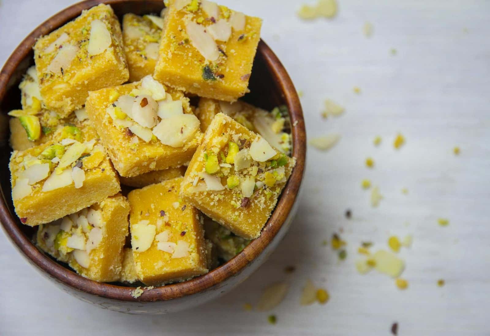 Kaju barfi Indian cashew-style sweets cut into squares with nuts and pistachios in a bowl
