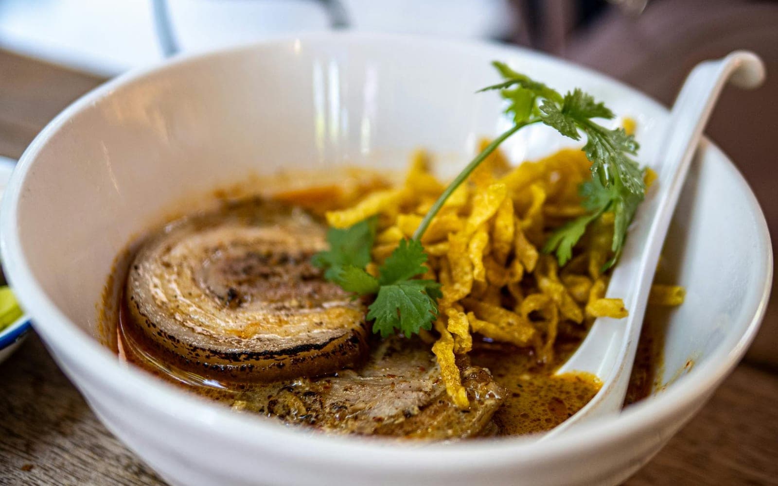 Khao soi curry noodles in a bowl with yellow curry broth, noodles, herbs, and crisp topping