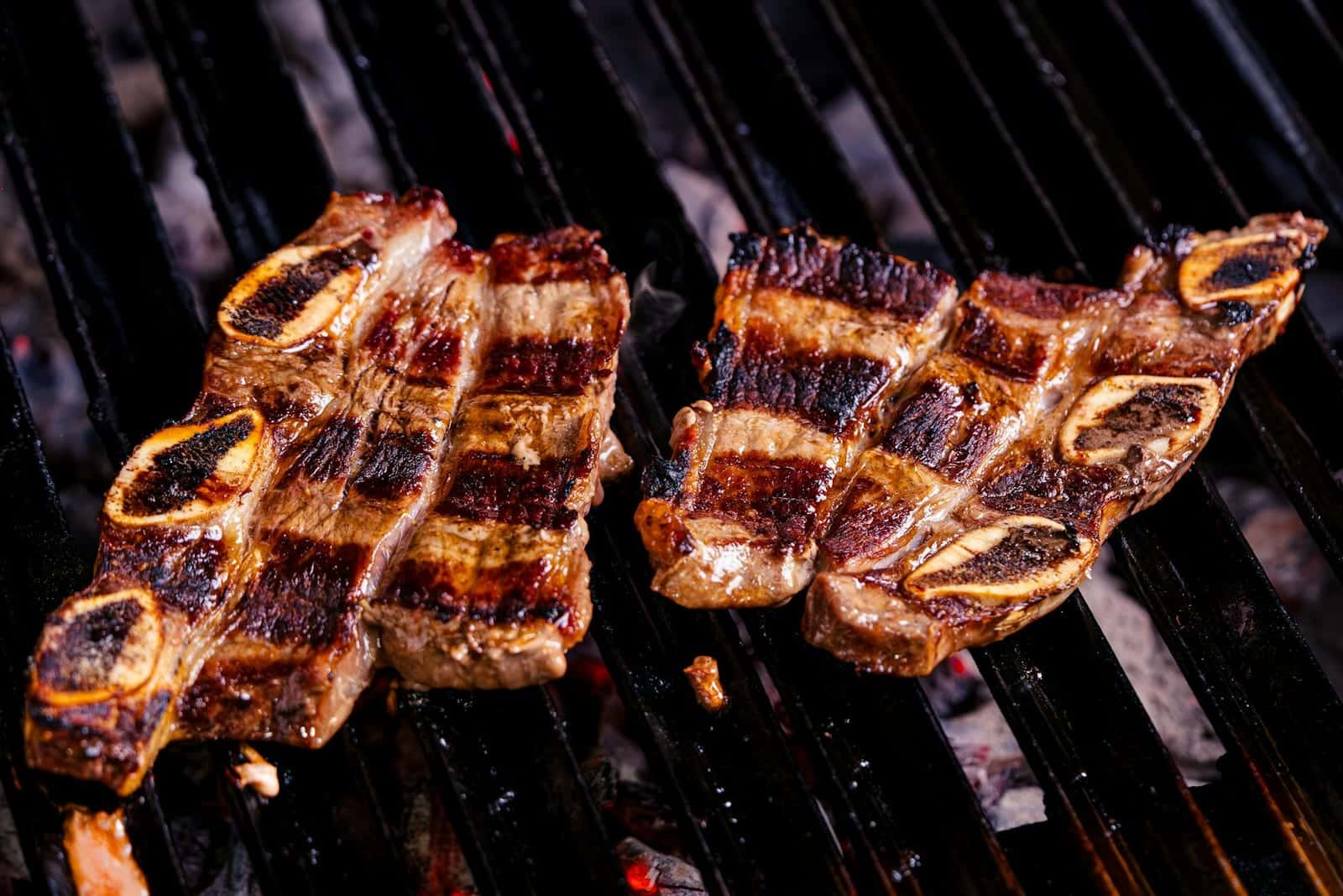 Korean BBQ short ribs grilling over charcoal with browned edges and visible grill marks