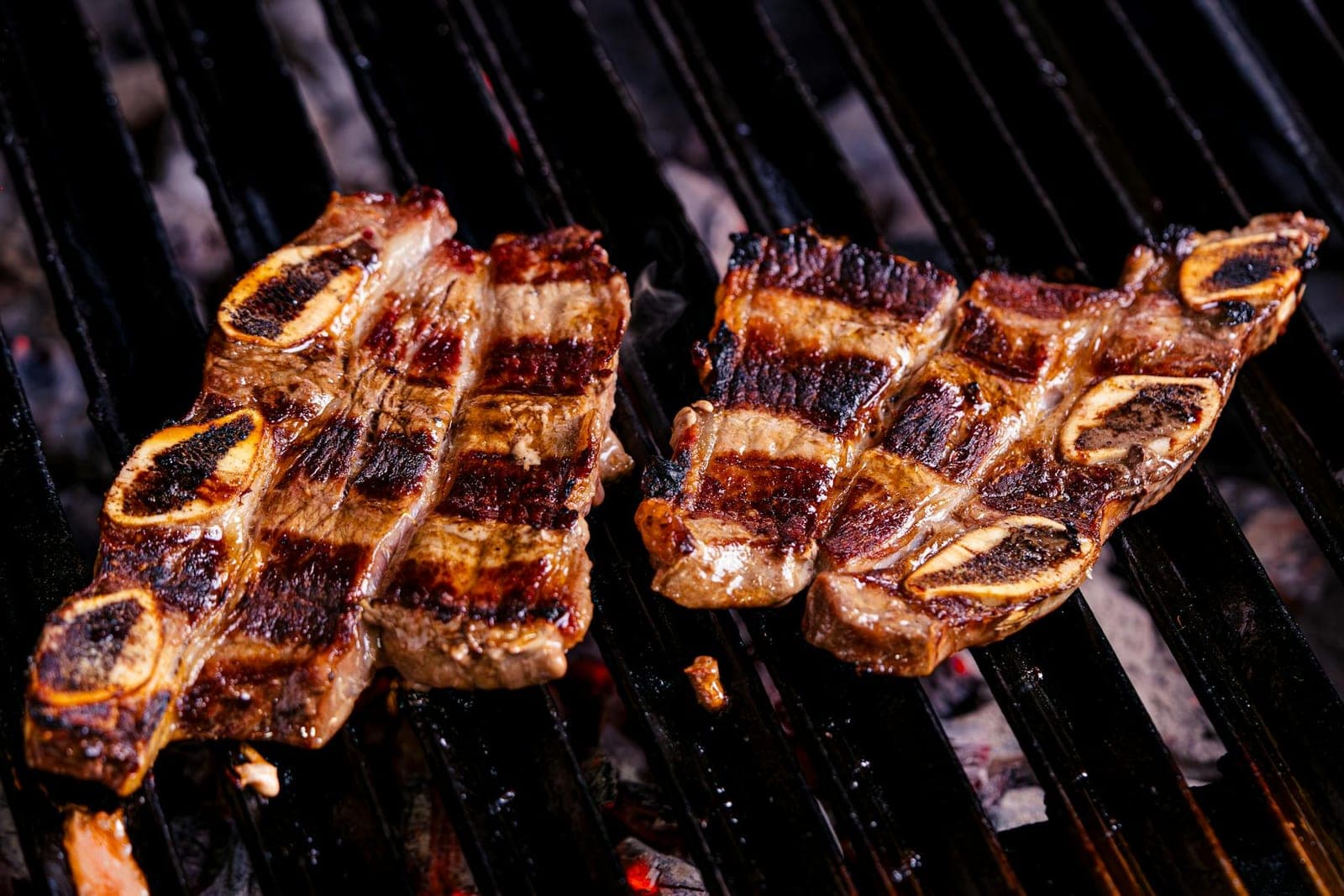 Korean BBQ short ribs grilling over charcoal with browned edges and visible grill marks