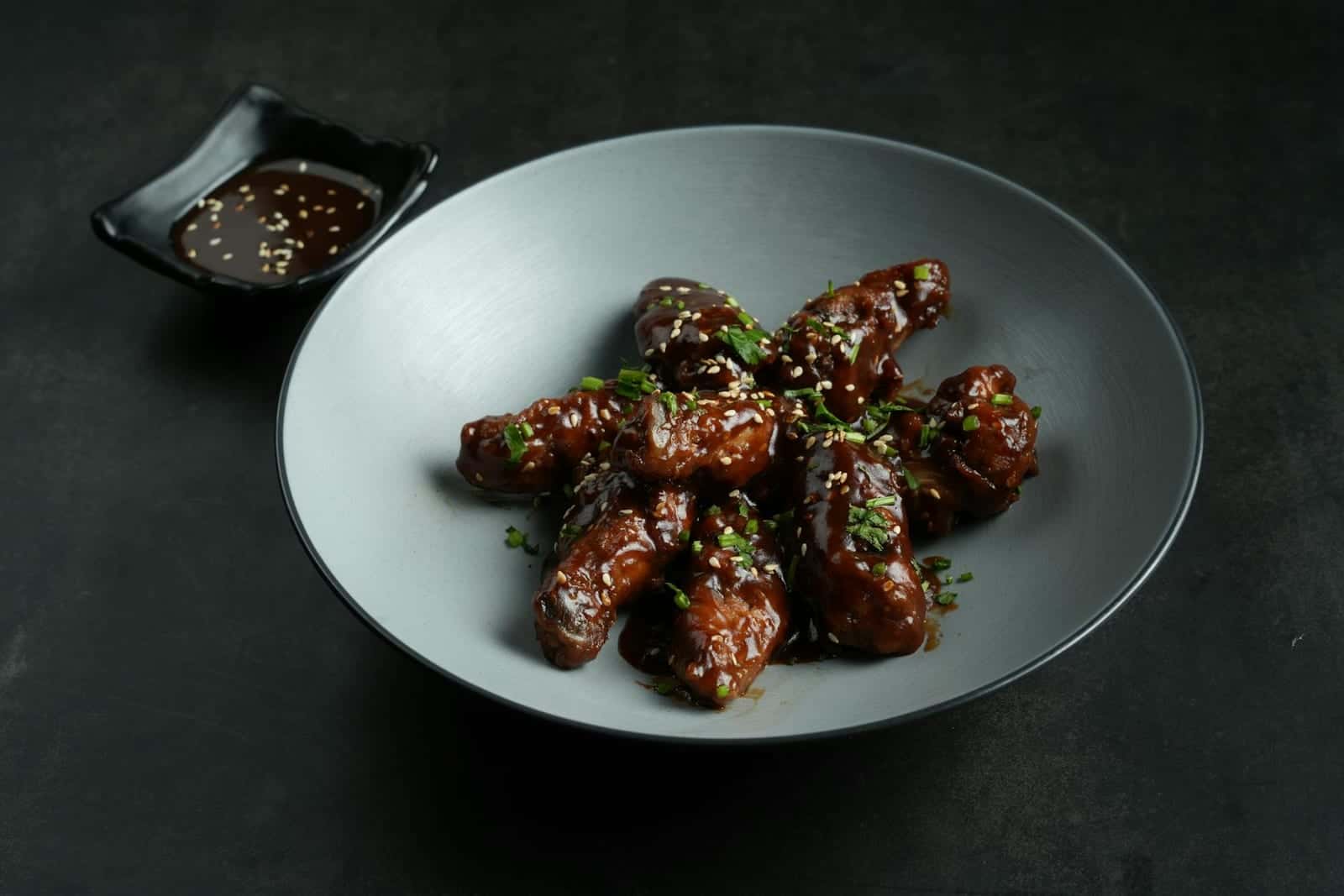 Korean fried chicken wings glazed with sauce and sesame seeds on a gray plate