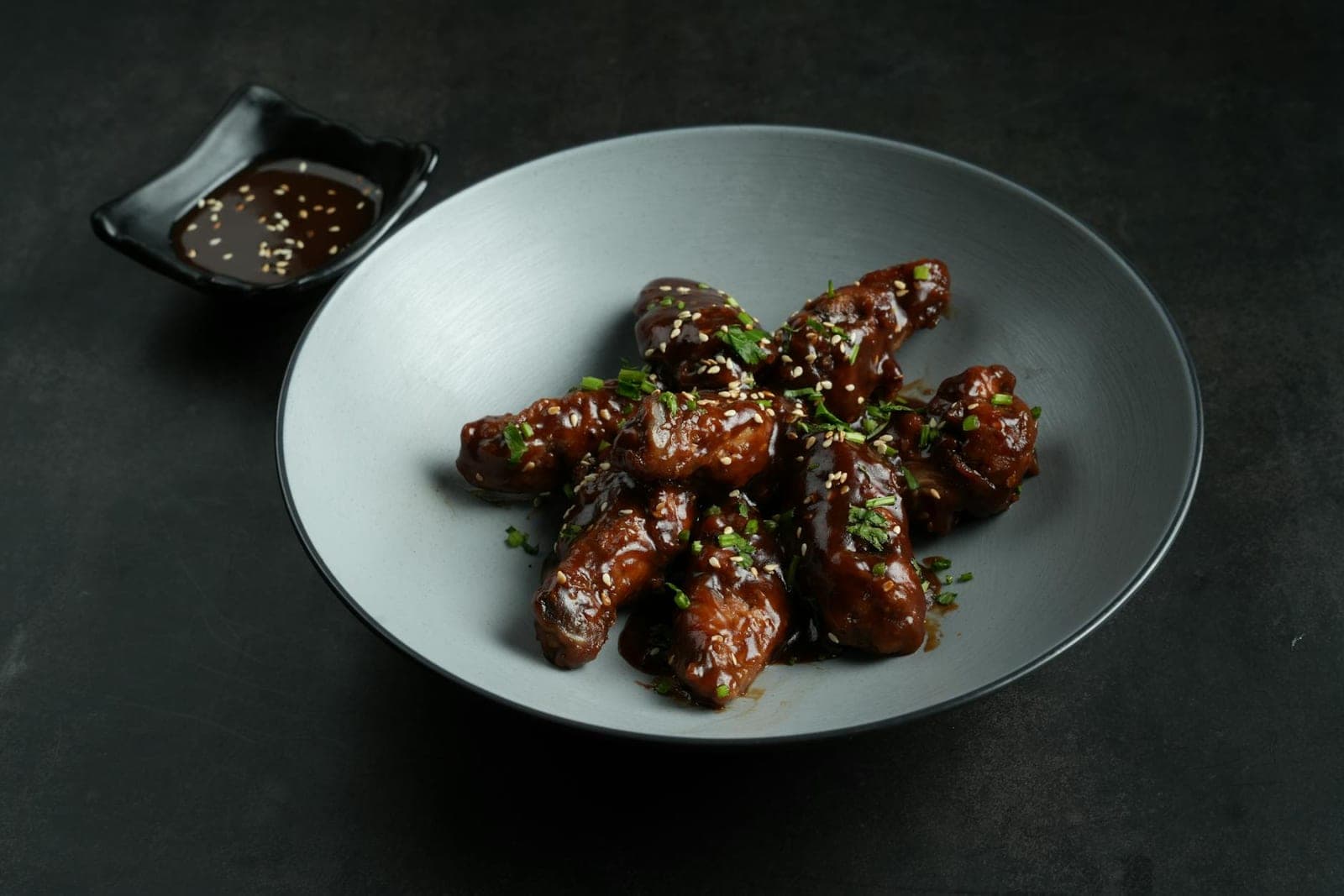 Korean fried chicken wings glazed with sauce and sesame seeds on a gray plate