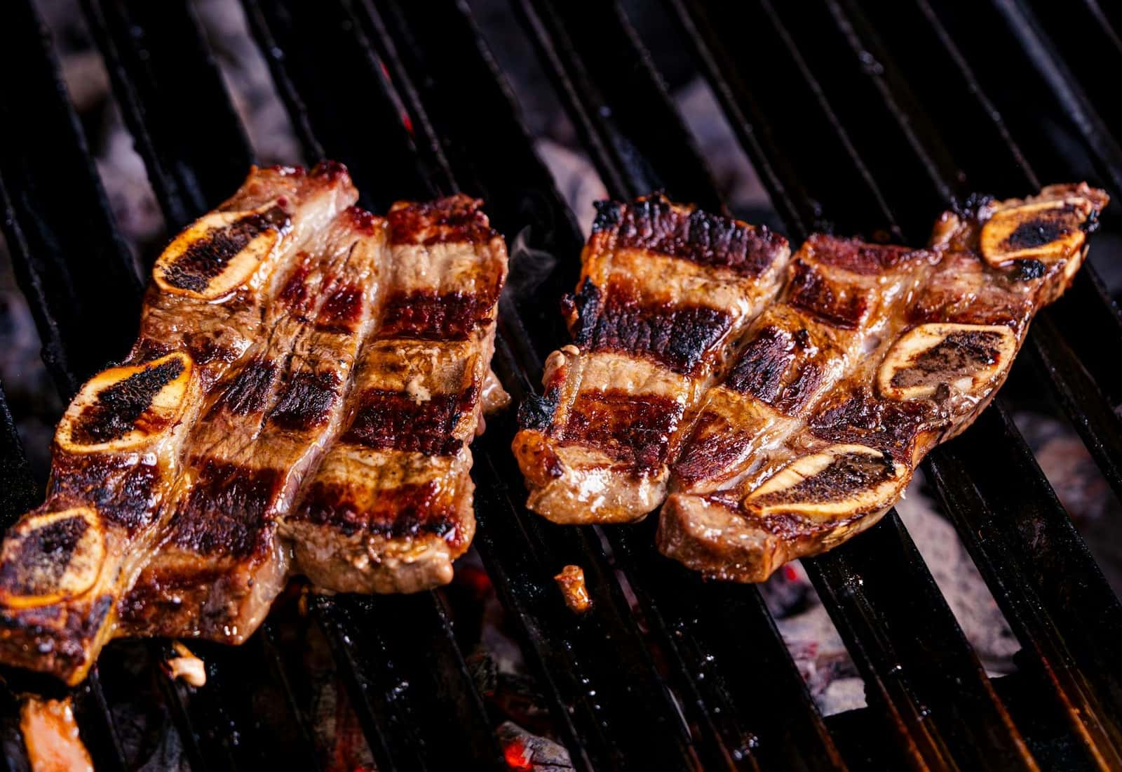 Korean galbi-style beef short ribs grilling over charcoal with deep sear marks
