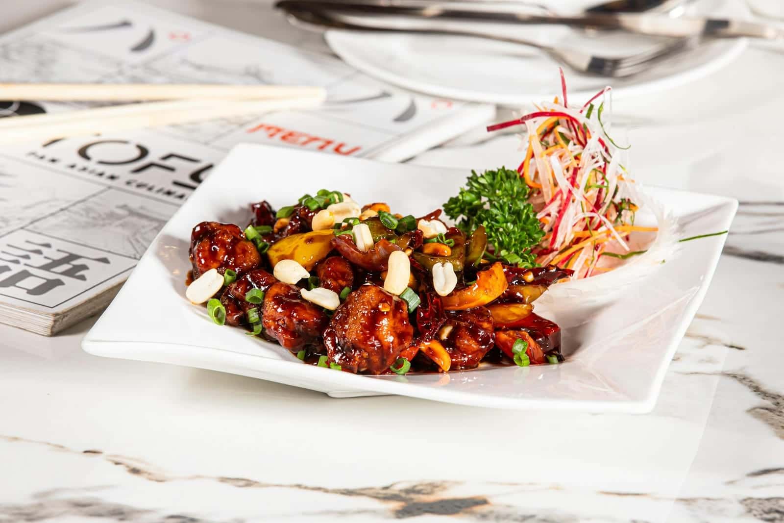 Kung Pao chicken with peanuts, chilies, scallions, and glossy sauce on a white plate