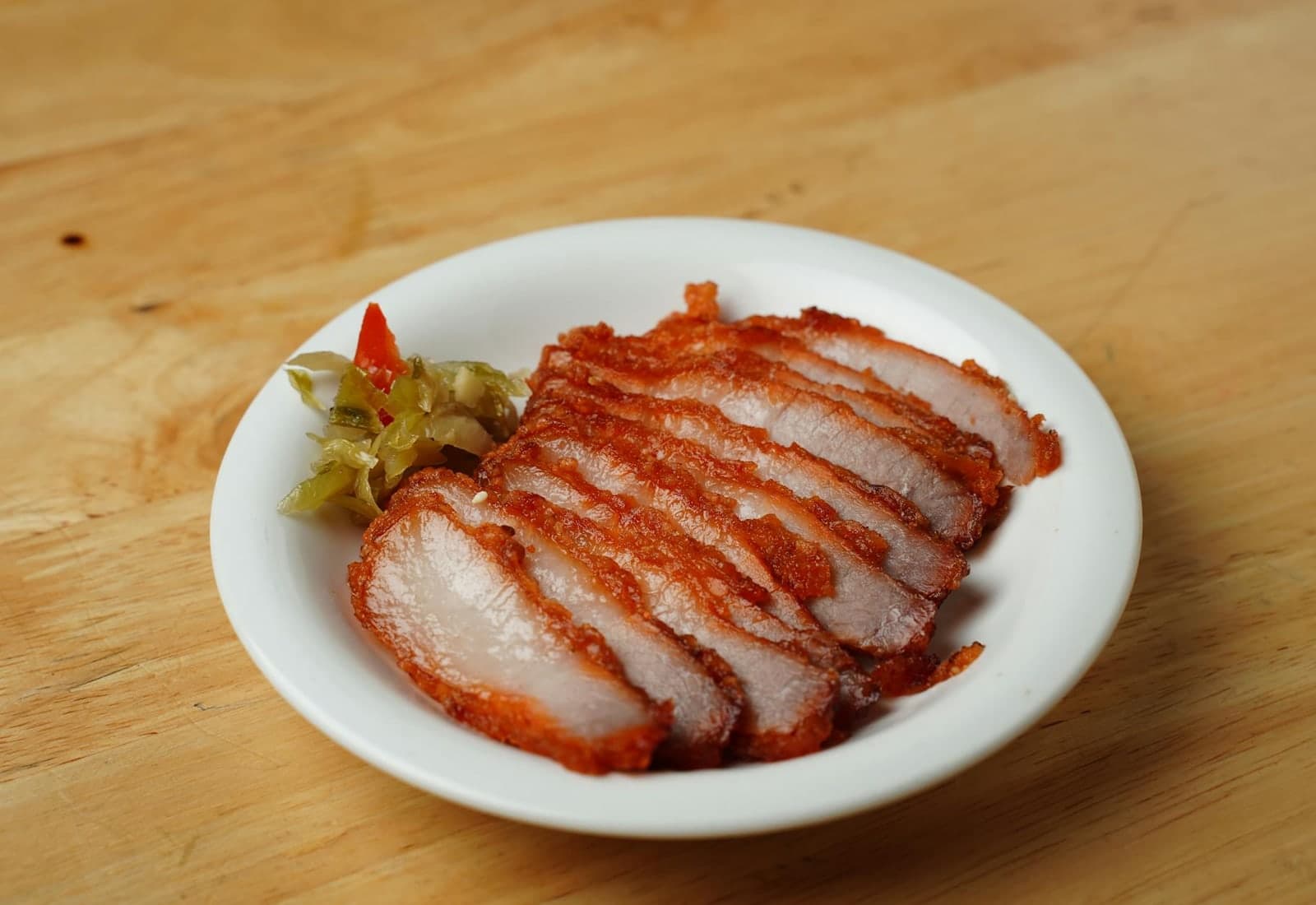 Lechon asado-style sliced roasted pork with pickled vegetables on a white plate