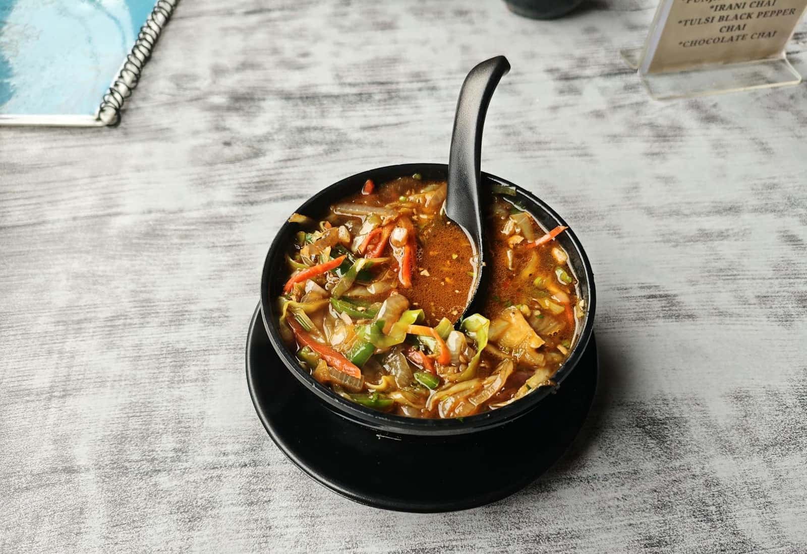 Manchow soup-style vegetable soup with noodles and vegetables in a black bowl