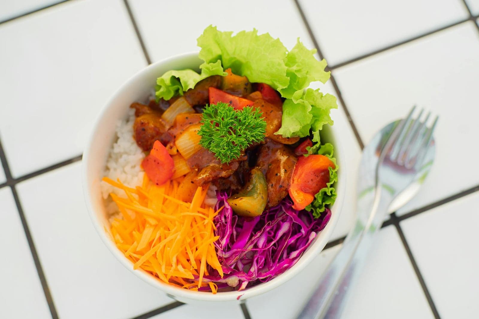 Mango chicken rice bowl with colorful vegetables, greens, and chicken in a white bowl
