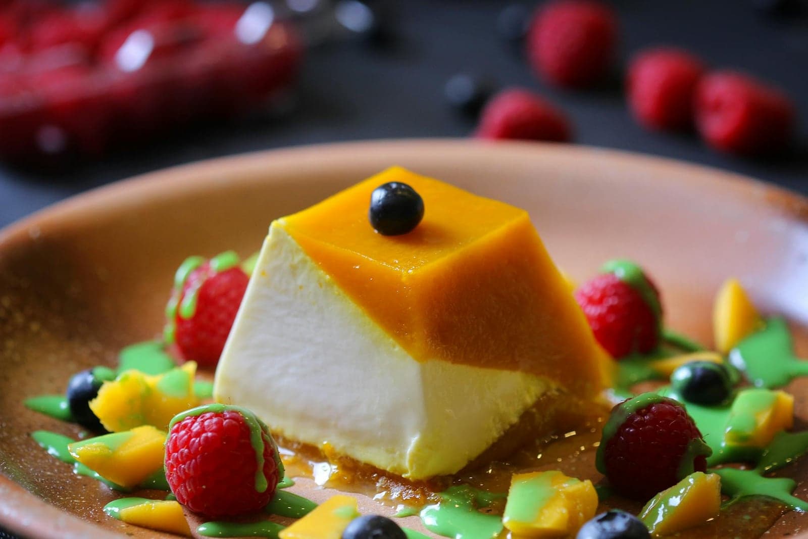 Mango coconut panna cotta with fruit sauce, berries, and a glossy mango topping